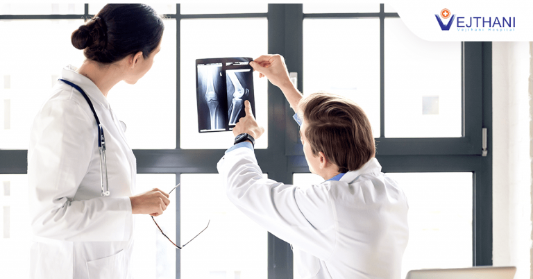 Two experienced orthopedic specialists analyze an x-ray of a knee joint.